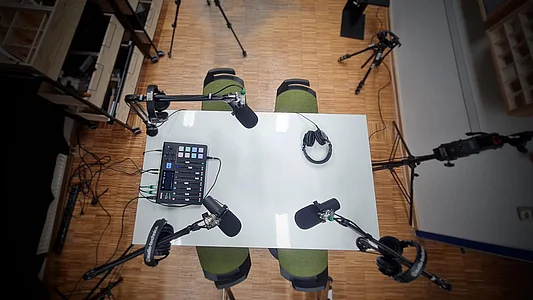 Vogelperspektive auf einen Tisch mit 4 Mikrofonen, an dem ein Podcast aufgenommen wird