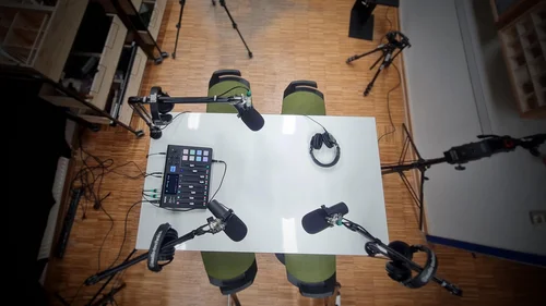 Vogelperspektive auf einen Tisch mit 4 Mikrofonen, an dem ein Podcast aufgenommen wird