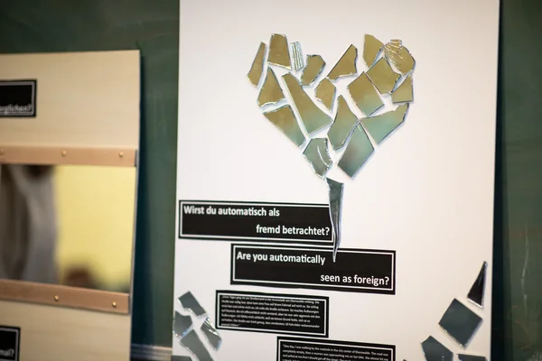 Im Bild ist ein Teil der Ausstellung zu (Alltags-) Rassismus zu sehen: ein Herz aus Spiegelscherben mit der Frage „Wirst du automatisch als fremd betrachtet?“ darunter.
