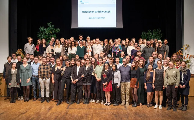Auf der Bühne im Haus Schwärzetal stehen die Alumni der Hochschule für nachhaltige Entwicklung Eberswalde aus dem Jahr 2023