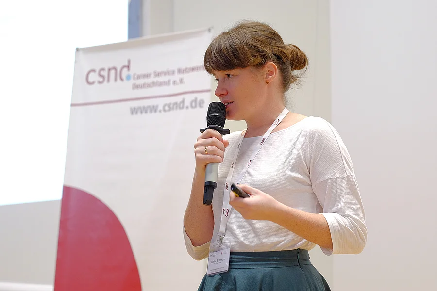 eine Frau steht auf der Bühne einer Tagung