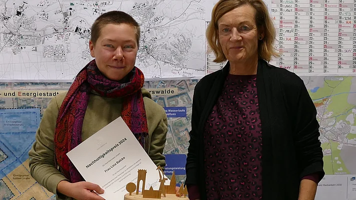 Links im Bild ist die Studentin Lina Balcke mit der Urkunde für den Nachhaltigkeitspreis 2024 der Stadt Eberswalde zu sehen. Rechts von ihr steht Sikle Leuschner, Leiterin Stadtentwicklung der Stadt Eberswalde. 